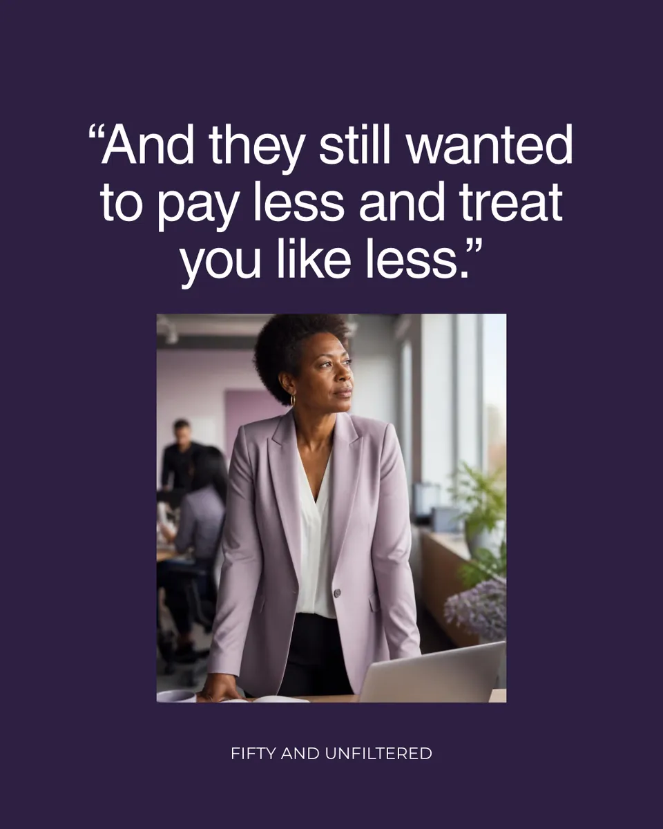 And they still wanted to pay less and treat you like less. A Black woman in her 50s in a lilac blazer stands at her desk in a busy office, looking out the window.